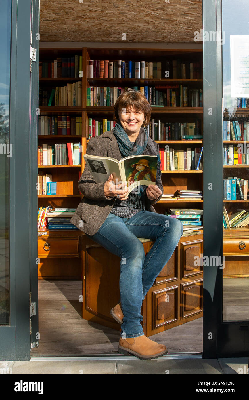 06 November 2019, Saxony, Reinhardtsdorf: Evelin Arnold sits on a stool in  the book stop in Reinhardtsdorf near Bad Schandau in Saxon Switzerland. The  former bus shelter was converted into a book