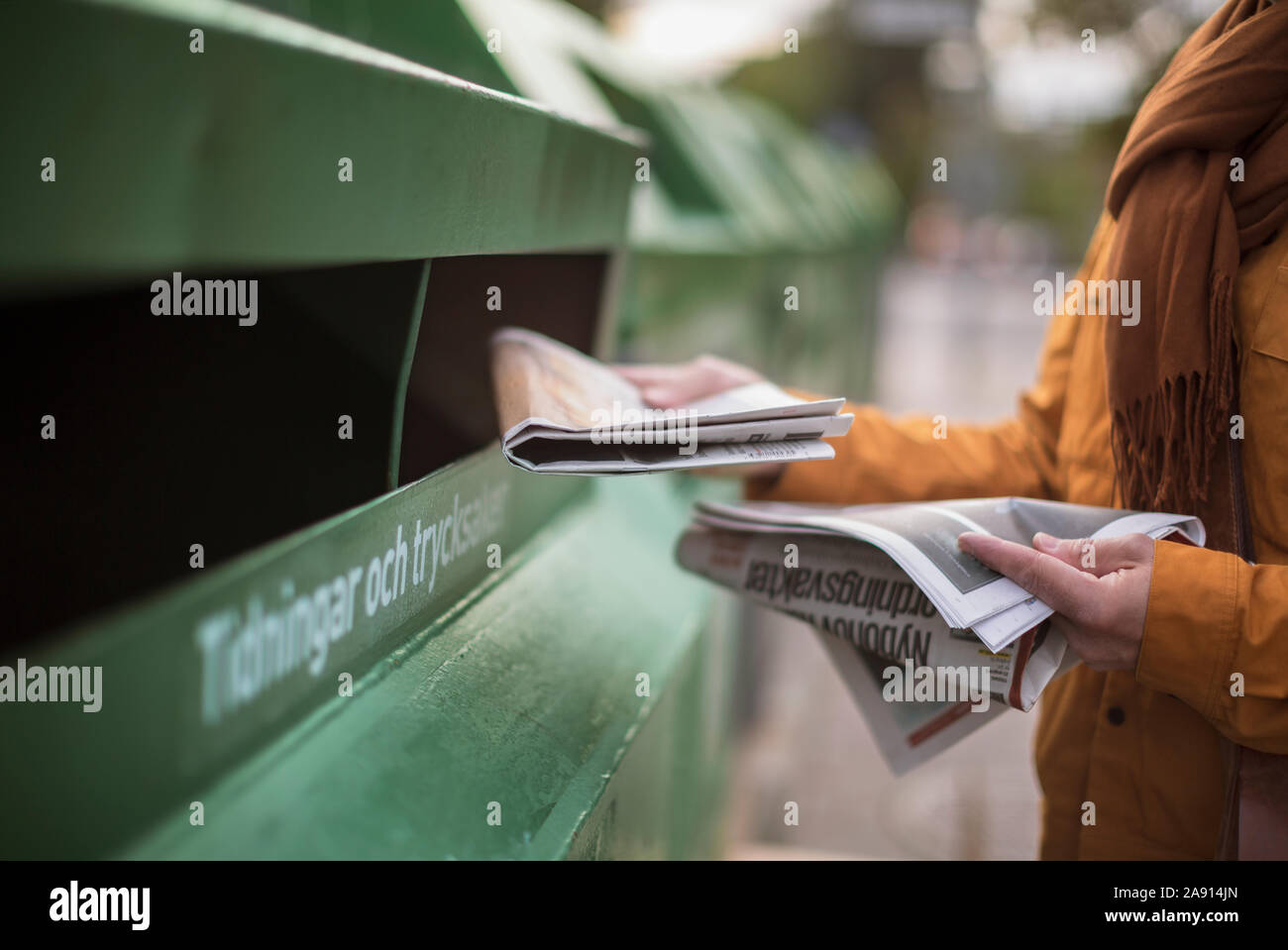 Hand putting newspaper into recycling bin Stock Photo