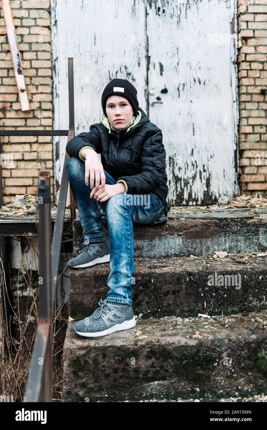 Teenage boy sitting at steps of abandoned building Stock Photo