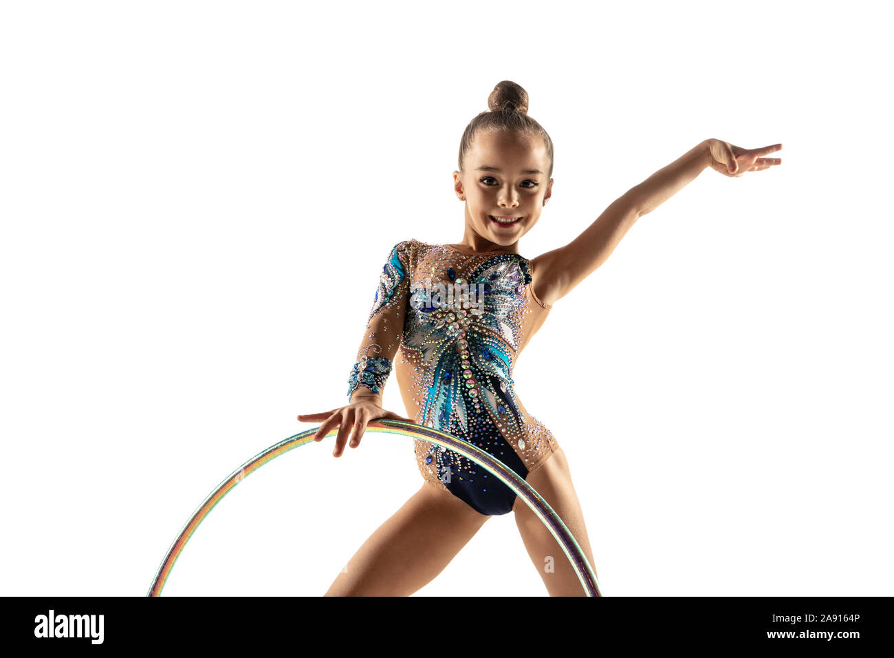 Little flexible girl isolated on white studio background. Little female model as a rhythmic gymnastics artist in bright leotard. Grace in motion, action and sport. Doing exercises with the hoop. Stock Photo