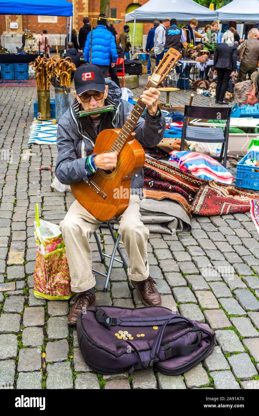 Old man playing guitar and mouth organ at flea market - Brussels, Belgium. Stock Photo