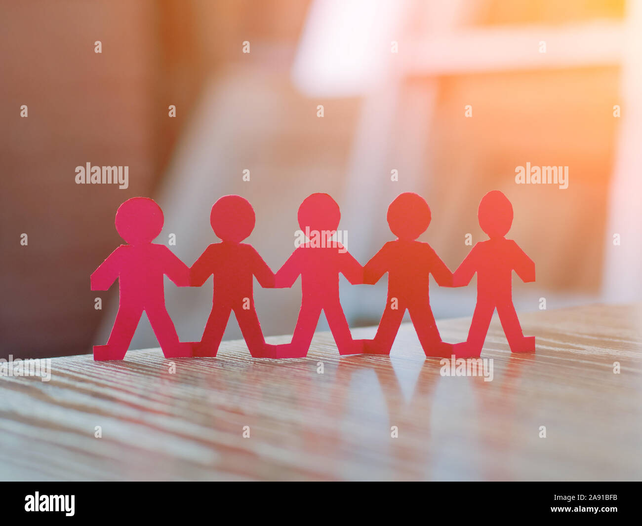 Team of paper chain people in a row on blurred background holding hands Stock Photo