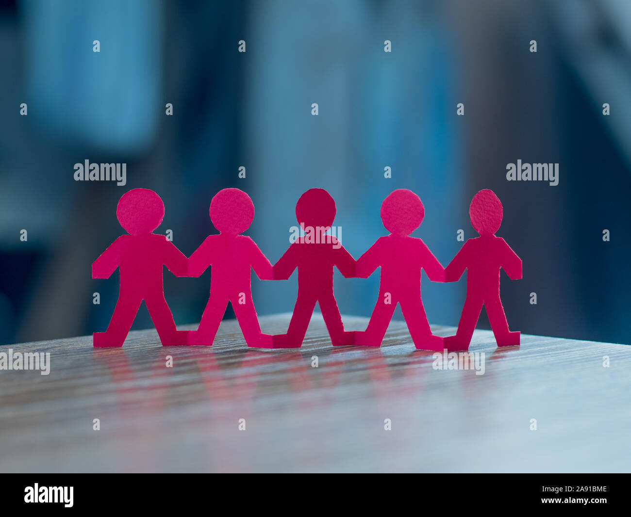 Team of paper chain people in a row on blurred background holding hands ...