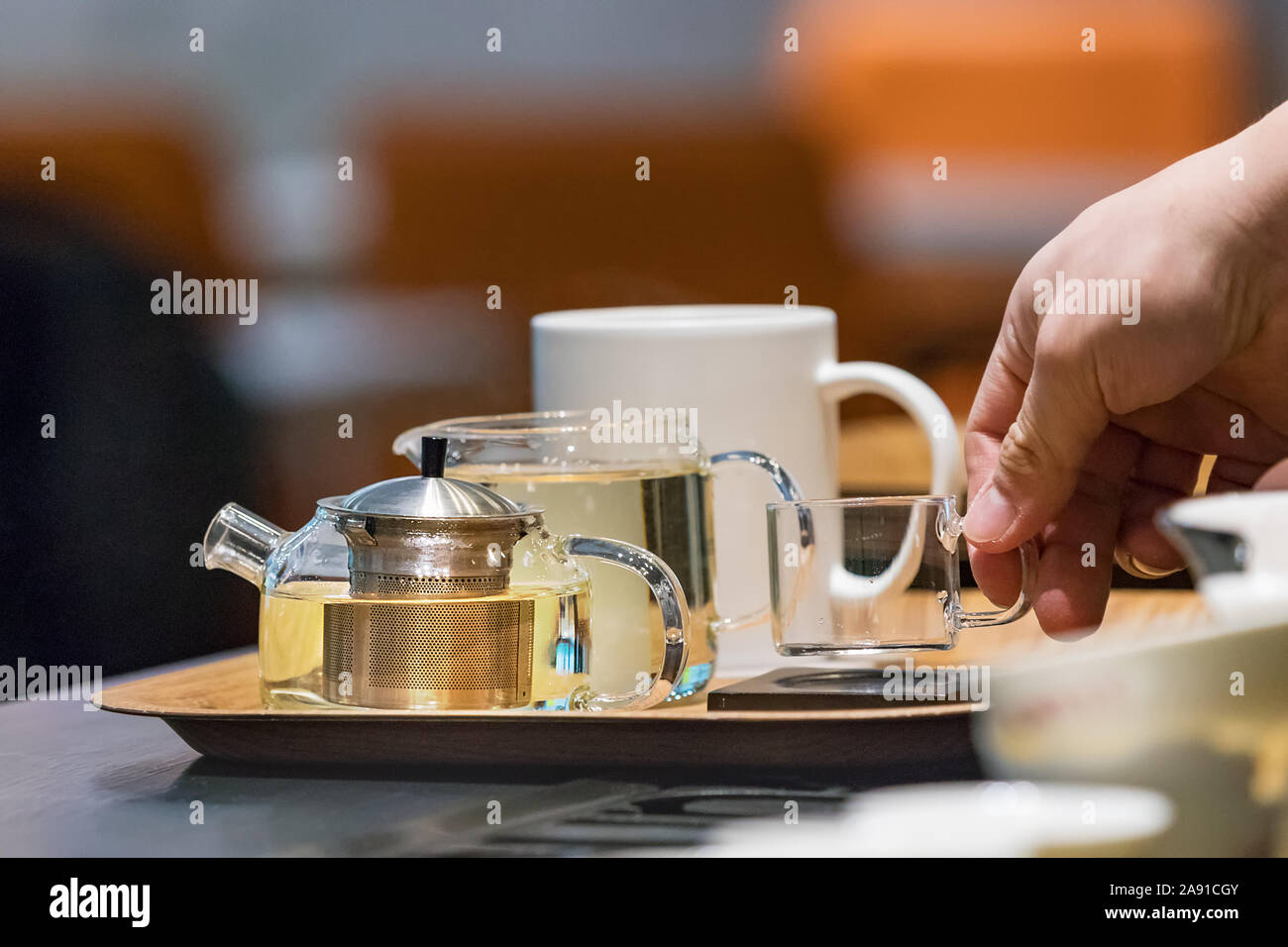 Barista male hands placing a glass cup on a tray with teapots at a