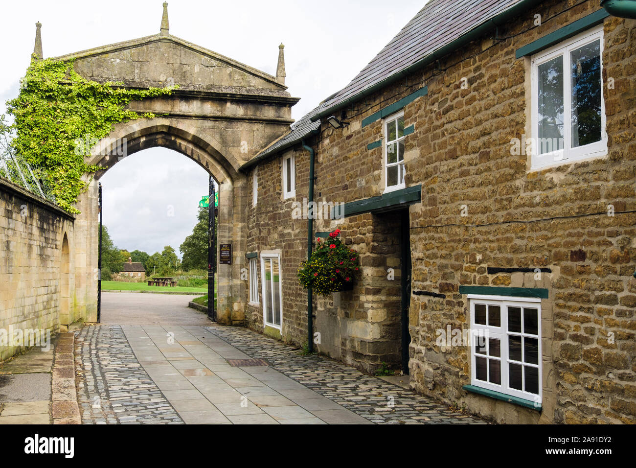 Old stone cottages on cobbled street leading to open arched gateway entrance to the castle. Oakham, Rutland, England, UK, Britain Stock Photo