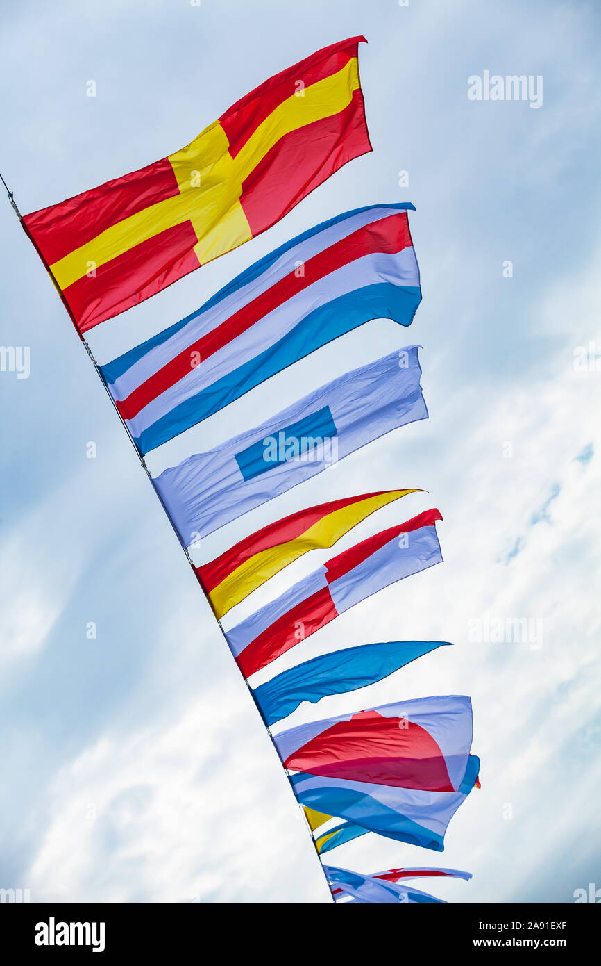 International maritime signal flags are waving on wind under blue cloudy sky, vertical photo Stock Photo