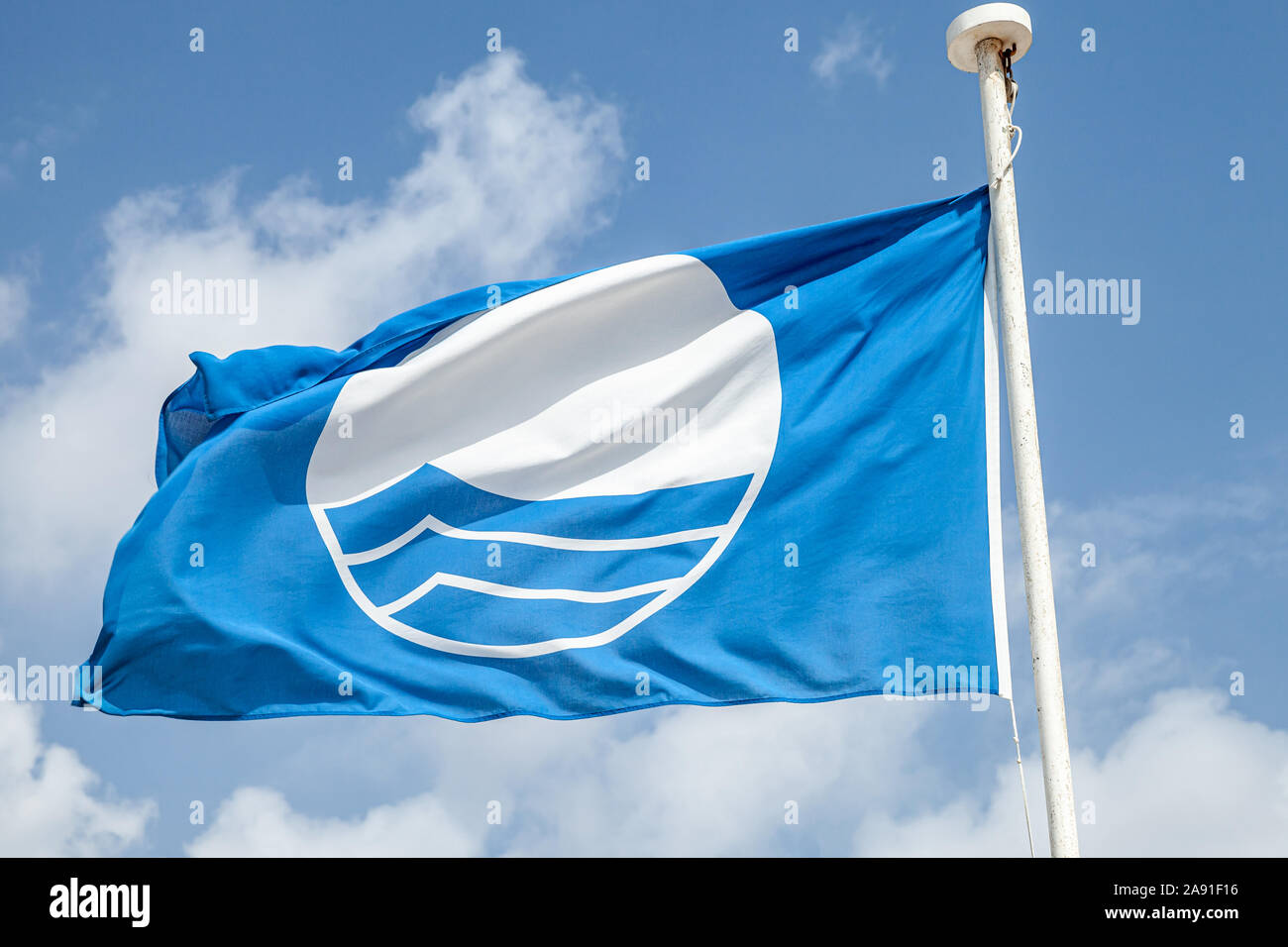 Blue Flag beach. Close-up photo of a flag waving under blue cloudy sky Stock Photo