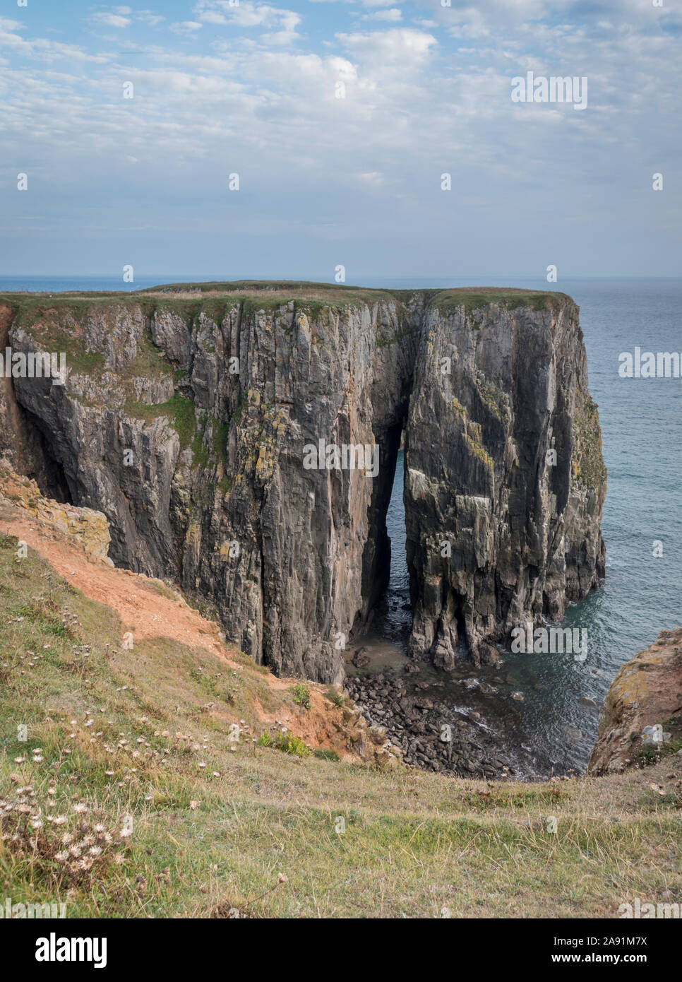 A natural arch in the rocks caused by coastal erosion on the shores of Pembrokeshire, Wales. Stock Photo