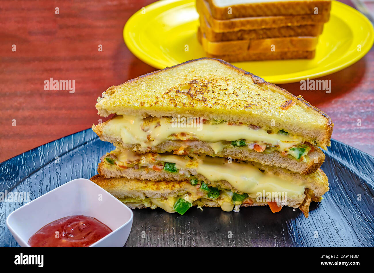 Three sets of stacked egg sandwiches with dripping cheese in a black plate along with ketchup and more slices in the background Stock Photo