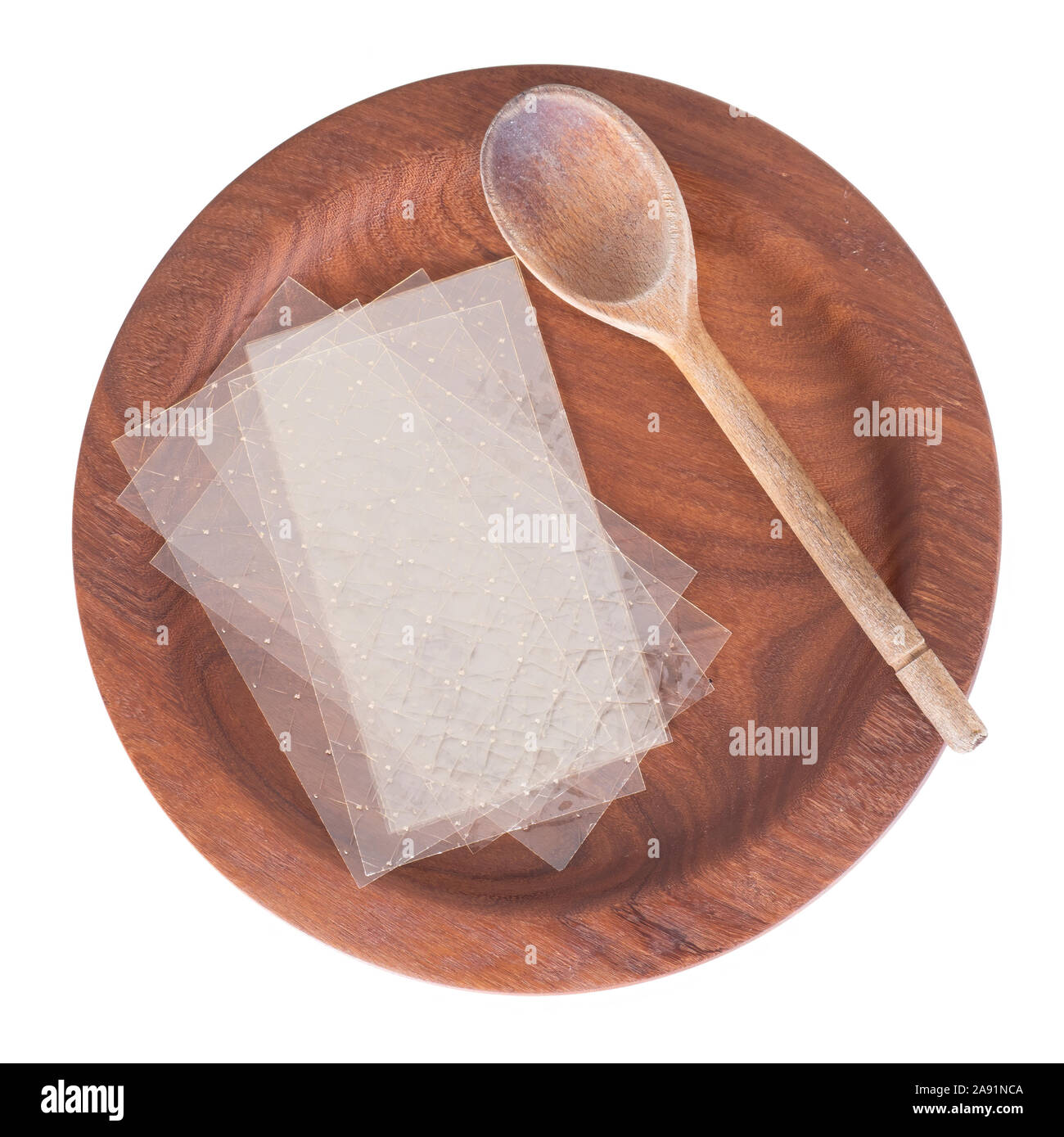 Sheets of colourless gelatin aka gelatine leaves on a wooden plate with spoon, isolated on white. Food ingredient. Stock Photo