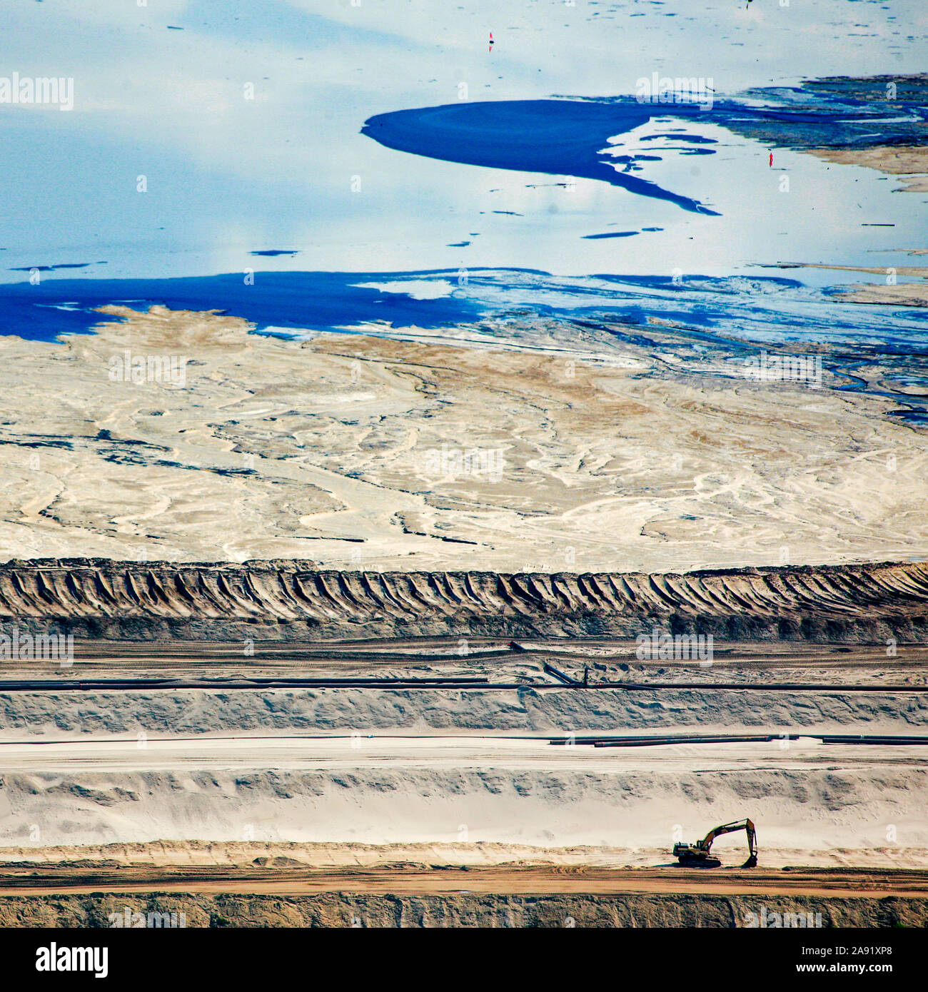 Bulldozers and earth movers are spreading the toxic waste in one of the enormous tailings ponds in Fort McMurray in Alberta, Canada. The ponds are among the largest man made structures in the world, spanning more than 175 square kilometres. They pose an added challenge to the oil sands production: even after ended production, it can take up to 30 years for the silt in the ponds to dry up. The contaminated water is toxic to any living creatures. The Athabasca oil sands deposit is among the largest in the world.  The bitumen, also commonly named tar (hence tar sands), contains lots of hydrocarbo Stock Photo