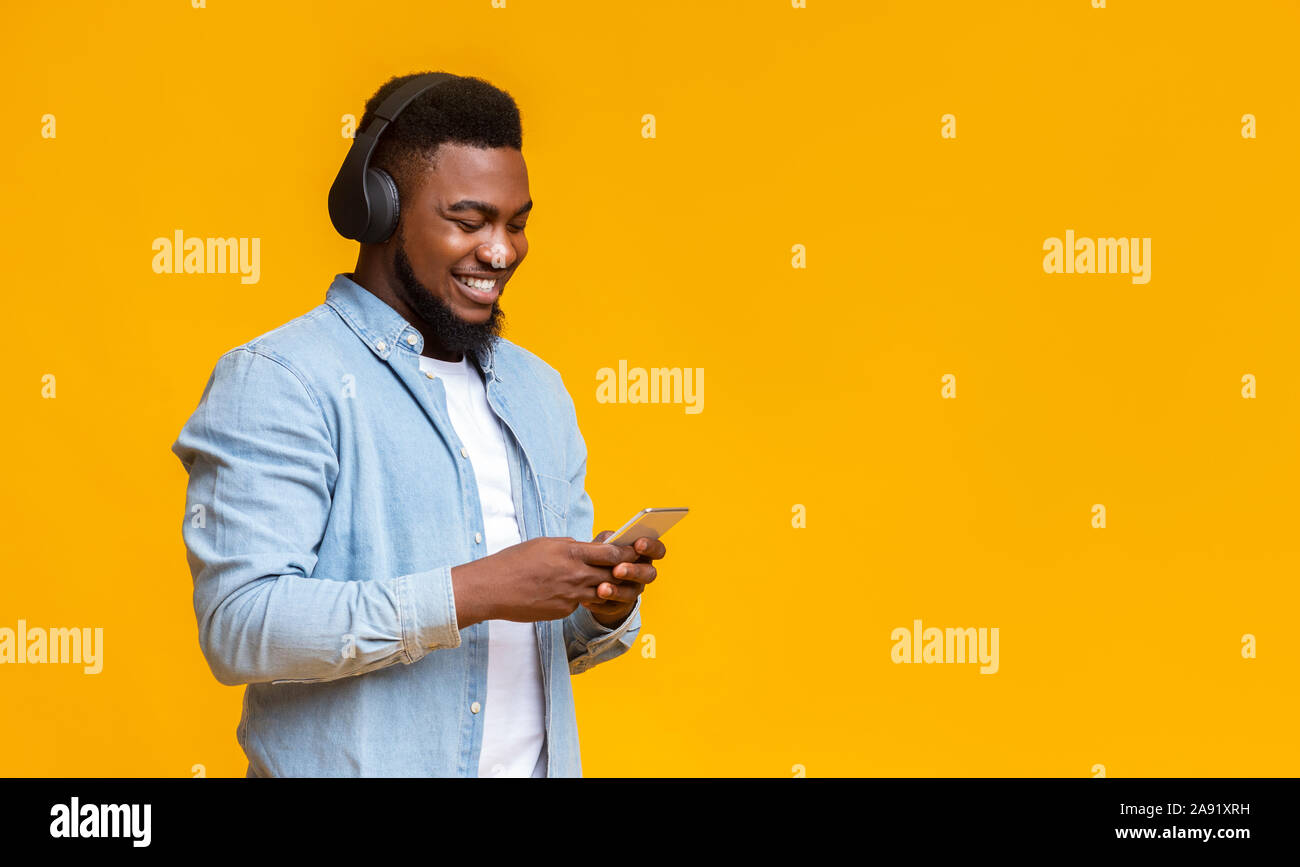 Cheerful millennial guy listening music on smartphone with wireless