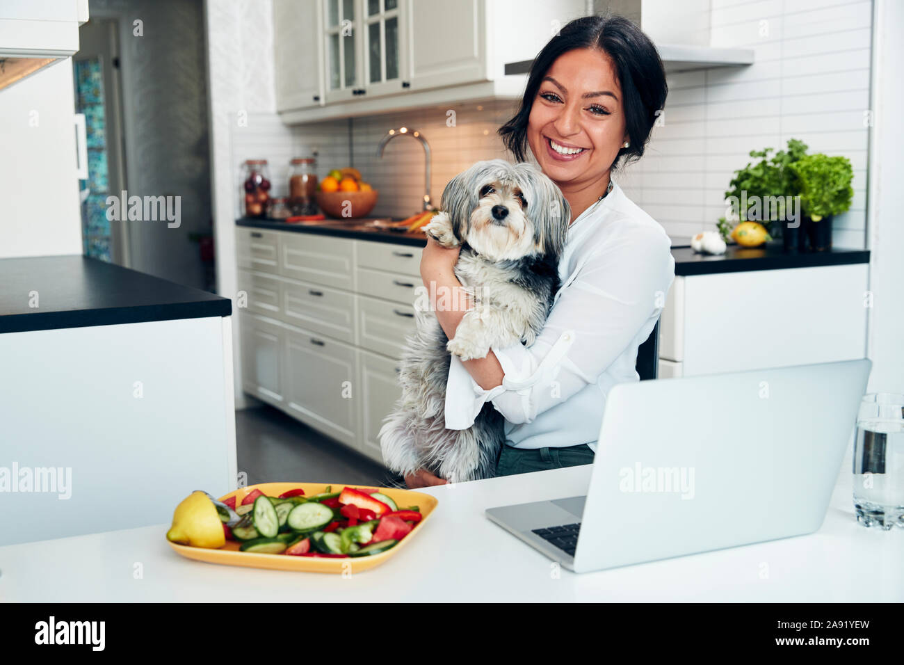 Smiling woman in kitchen holding dog Stock Photo
