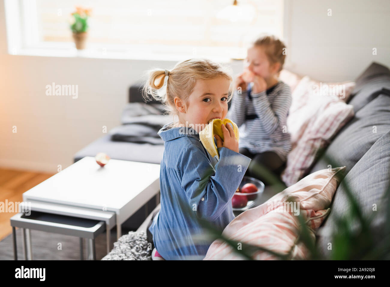 Girl eating banana on sofa Stock Photo