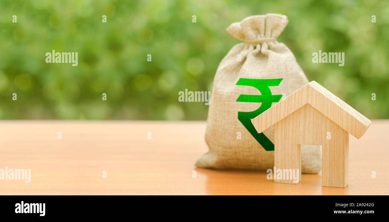 Wooden house figurine and a money bag with a Indian rupee symbol. Mortgage loan for the purchase of housing. Down payment first installment on the loa Stock Photo