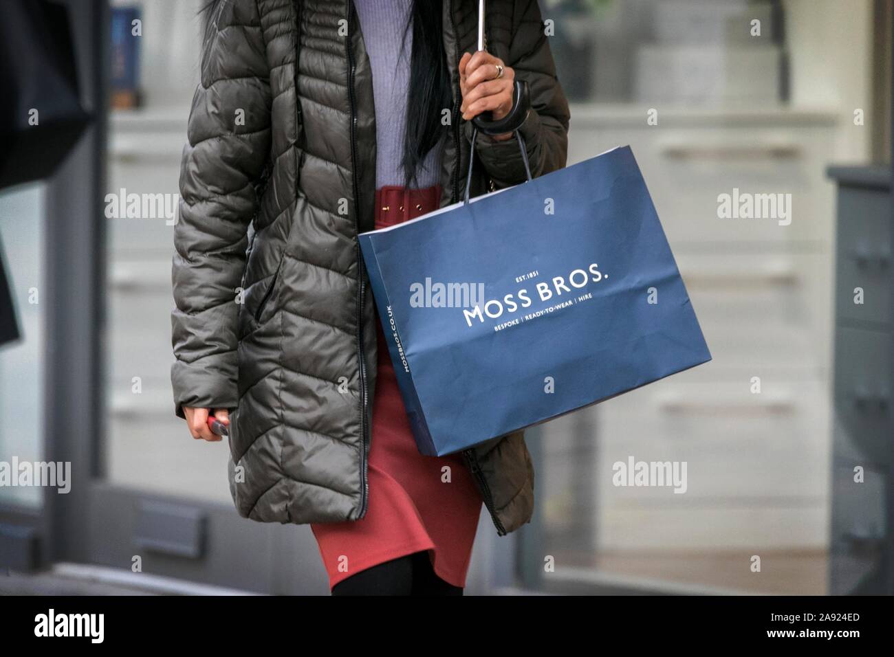 A woman carrying a paper Moss Bros mens clothing store carrier bag in Preston, Lancashire, UK Stock Photo