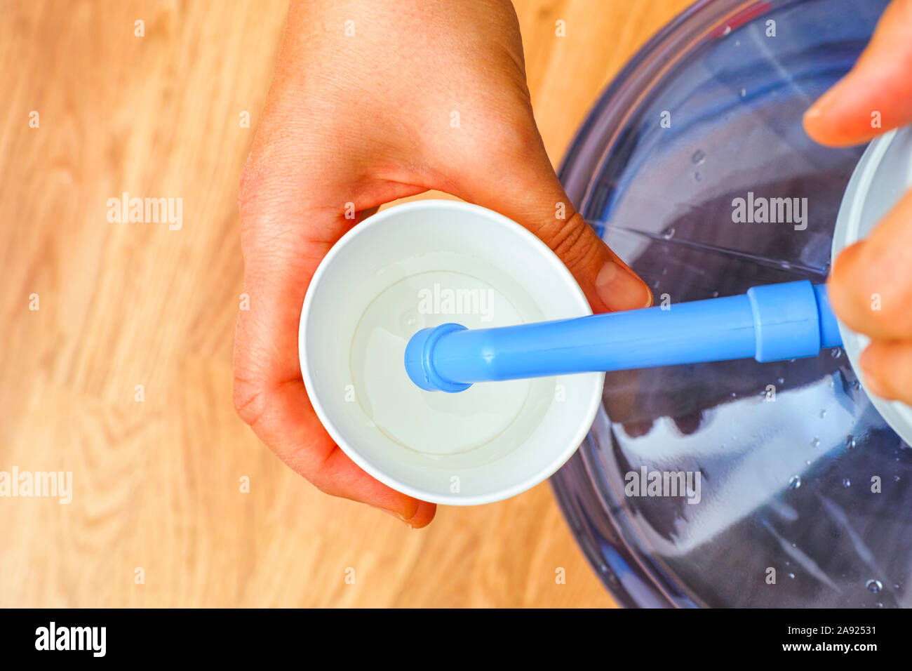 Woman hands pouring water in paper cup from bottle with water pump. Top