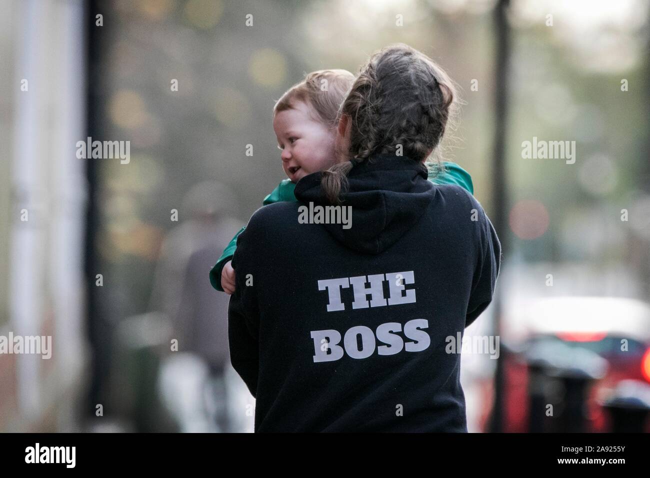 A woman carries her toddler child whilst wearing The Boss hoodie in Preston, Lancashire, UK Stock Photo