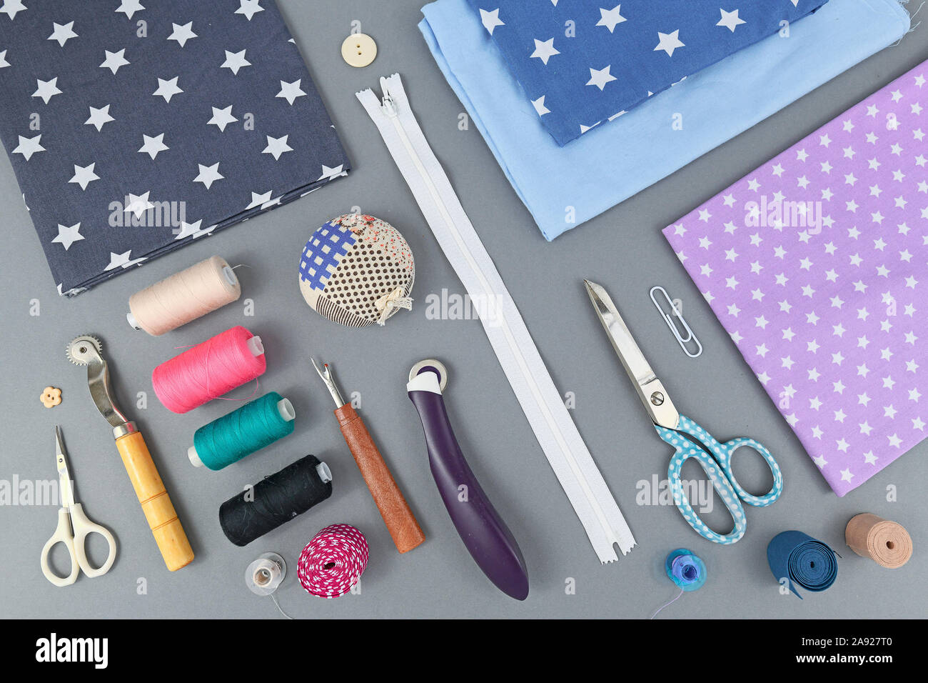 Overhead flat lay with various different sewing tools like fabric, thread, zipper, scissors, spool, thread seperator, pincushion or rotary cutter on g Stock Photo