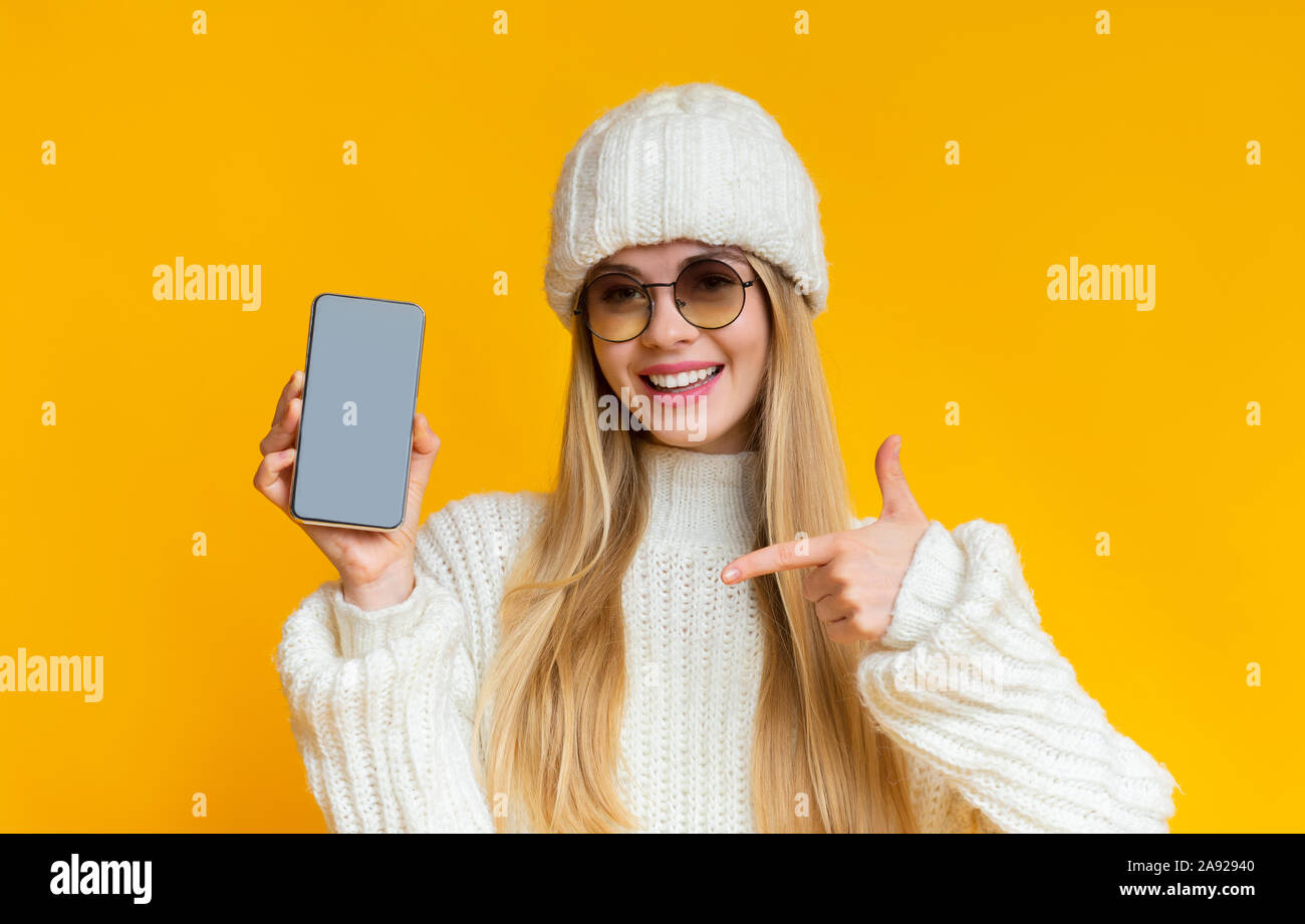 Woman in winter hat pointing at blank smartphone screen Stock Photo
