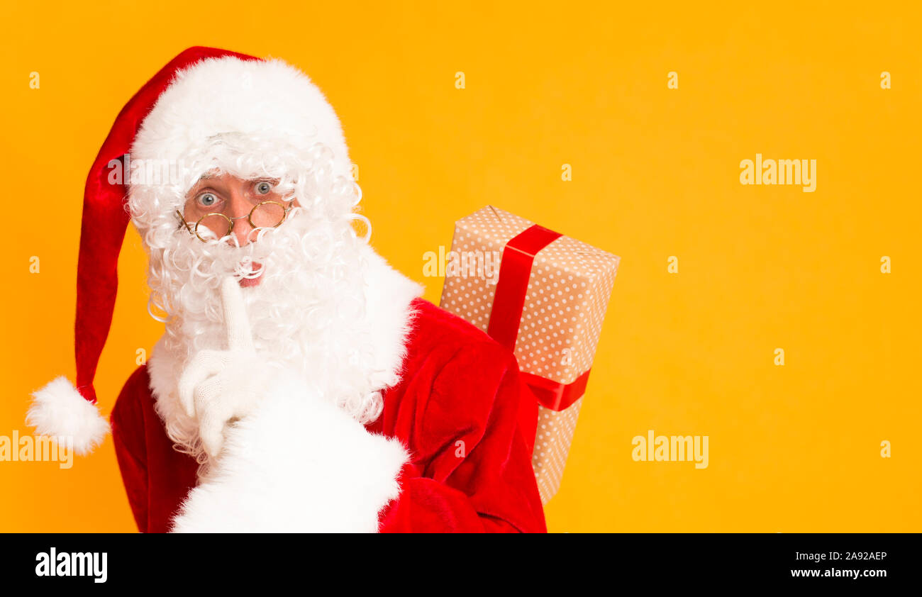 Santa holding finger near mouth and hiding Christmas gift Stock Photo