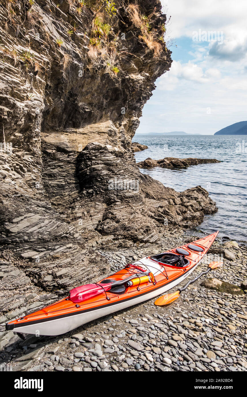 A sea kayak and paddles on a rocky beach, Orcas Island, Washington, USA. The Rosario Strait in the distance. Stock Photo