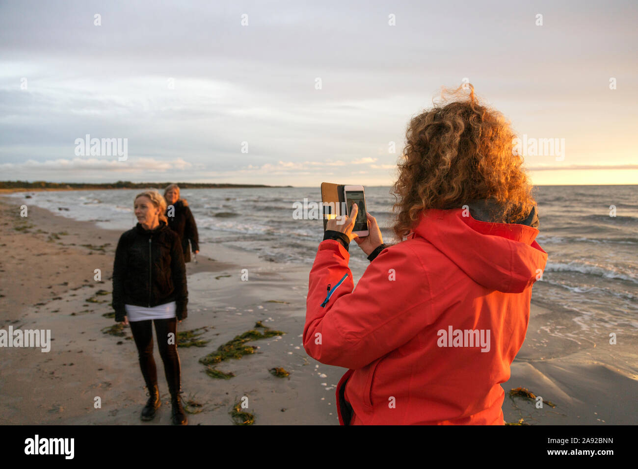 woman photographing friends on the beach with her smartphone Stock Photo