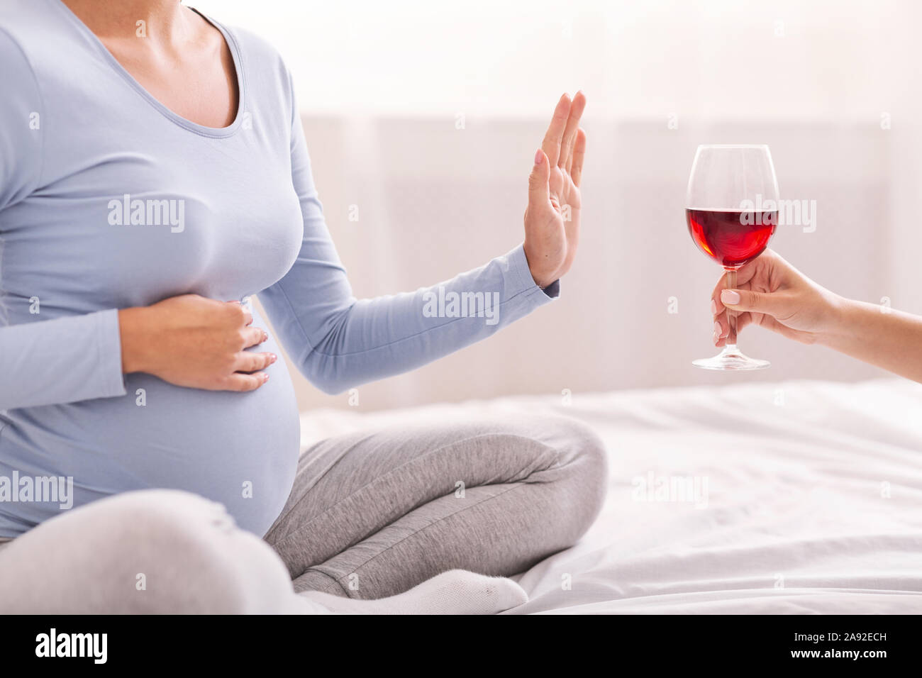Unrecognizable Pregnant Girl Refusing To Take Wine Sitting On Bed Stock Photo