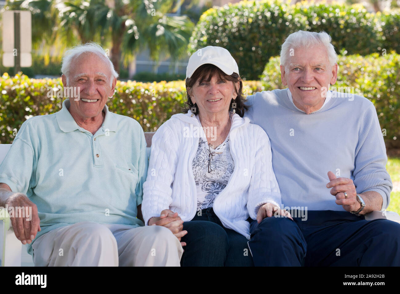 Three senior friends sitting on a park bench and smiling Stock Photo