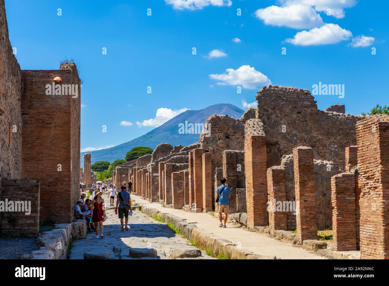 Tourists walk through the excavated ruins down a street in Pompeii with Mount Vesuvius in the background; Pompeii, Province of Naples, Campania, Italy Stock Photo