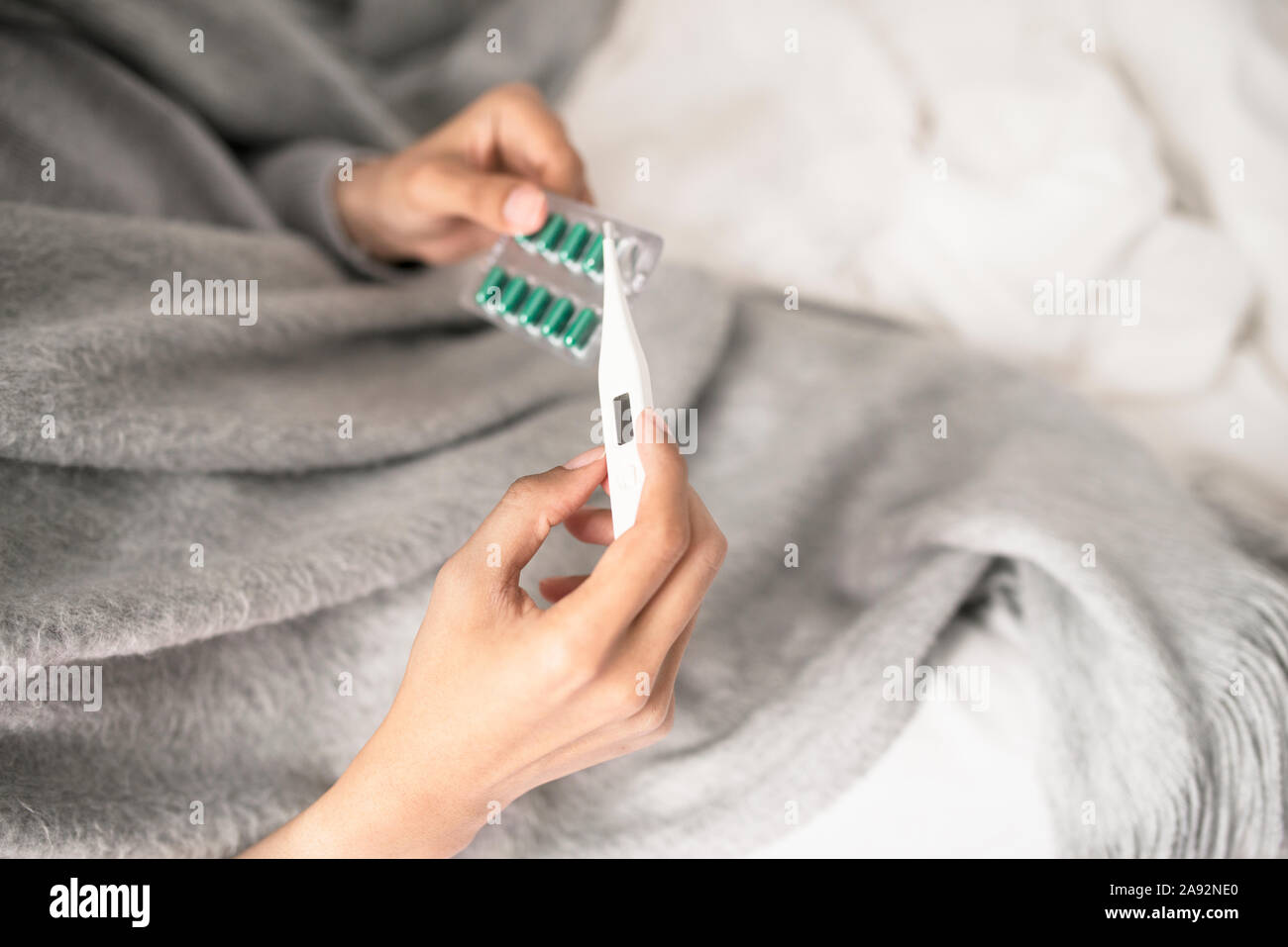 Man holding thermometer and pills in bed Stock Photo