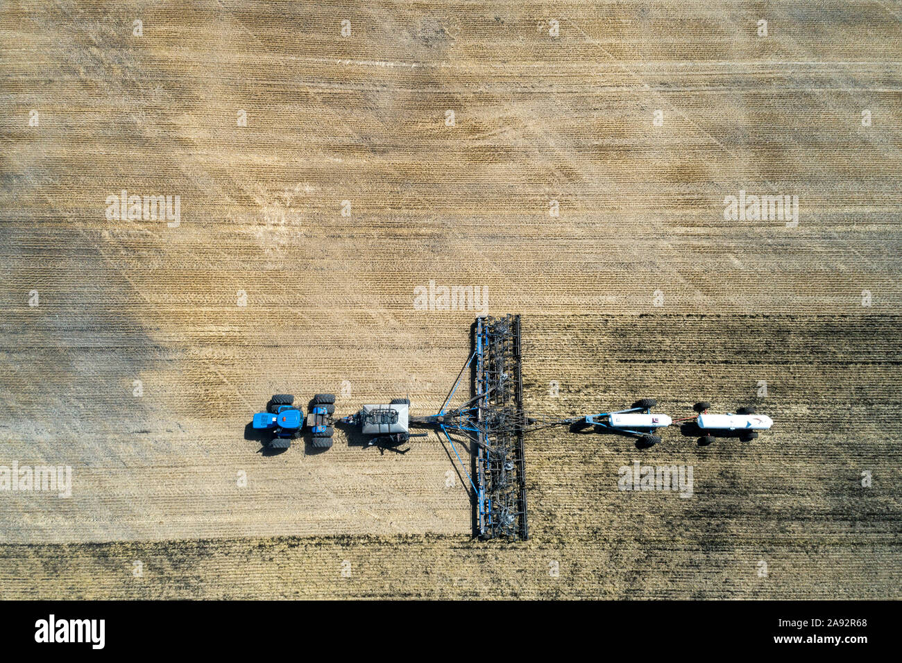 Aerial view of air seeder in field with white ammonia tanks, near Beiseker; Alberta, Canada Stock Photo