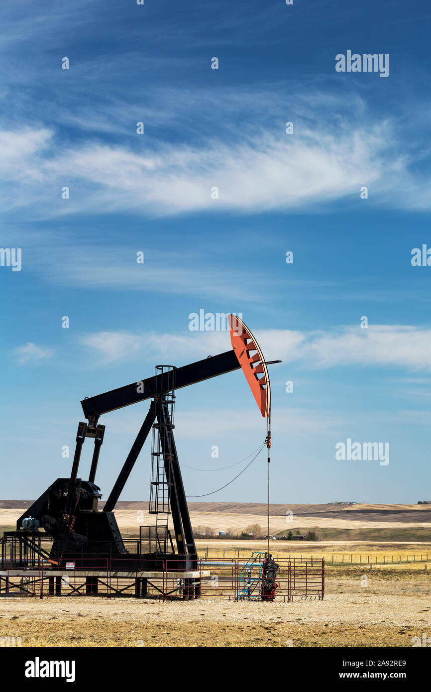 Pumpjack in field with rollings hills, clouds and blue sky in the background, West of Airdrie; Alberta, Canada Stock Photo