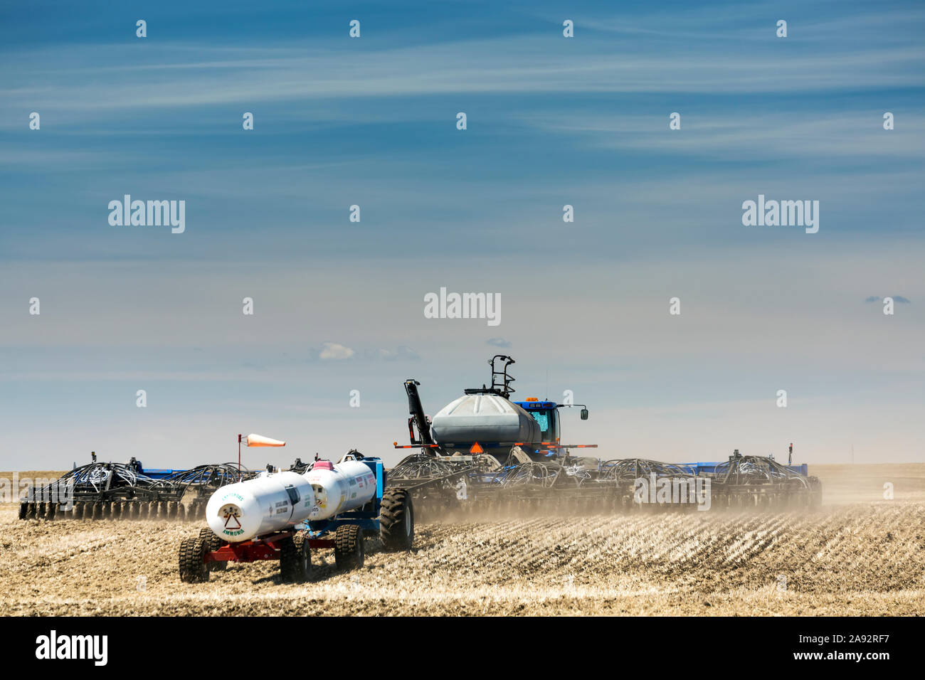 Air seeder in field with white ammonia tanks, near Beiseker; Alberta, Canada Stock Photo