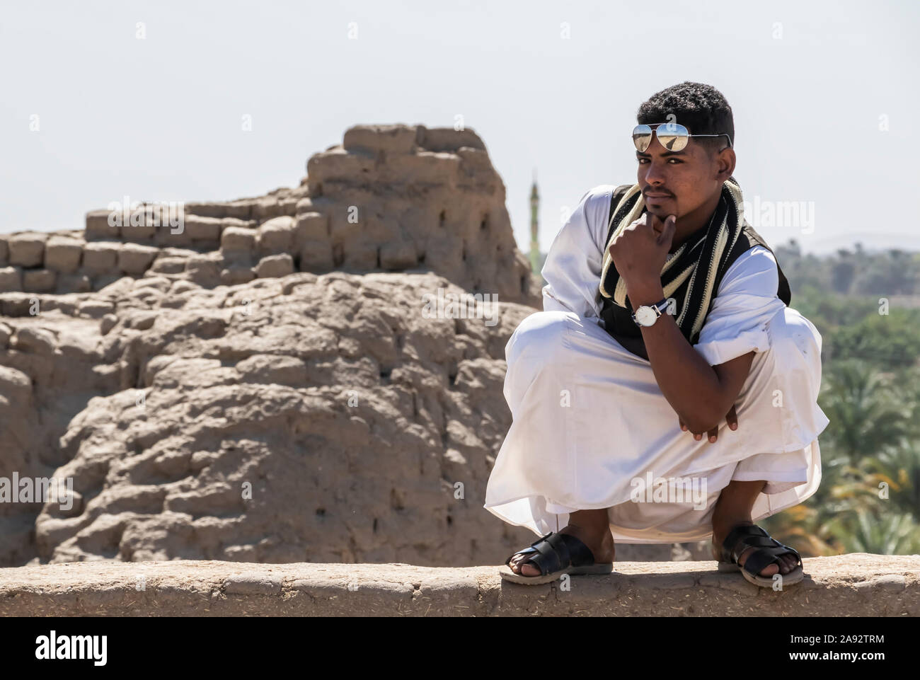 Young Sudanese man posing with confidence while crouching on a rock wall; Kerma, Northern State, Sudan Stock Photo
