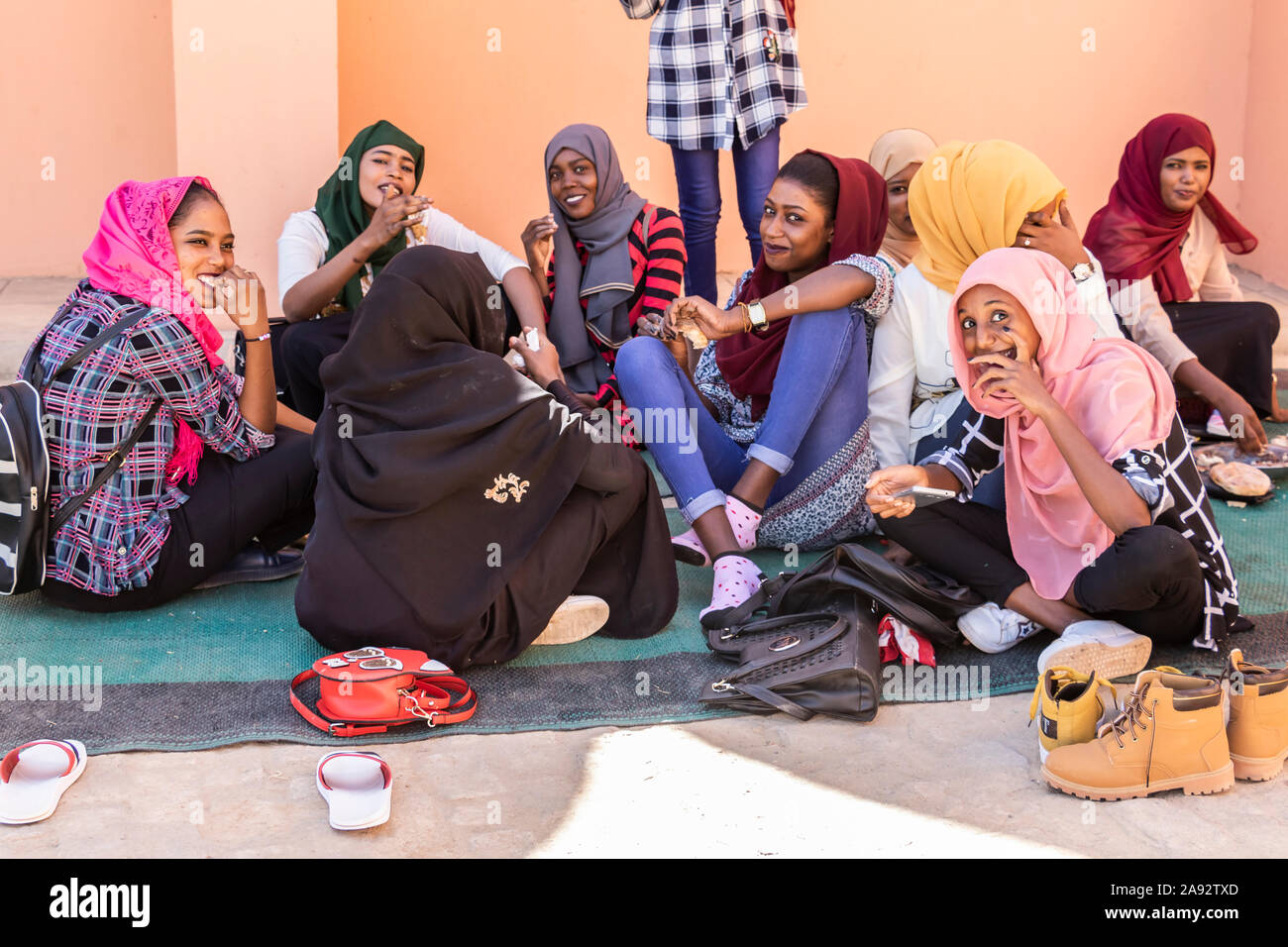 Young Sudanese women sitting on the ground visiting and eating together; Kerma, Northern State, Sudan Stock Photo