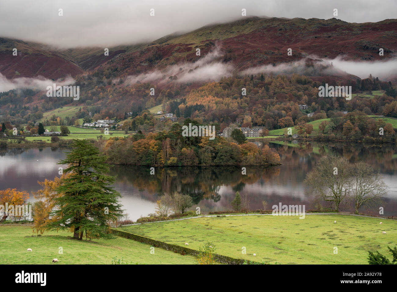 Mist and low cloud hanging over Grasmere island in the middle of Grasmere lake on a rainy autumnal day Stock Photo