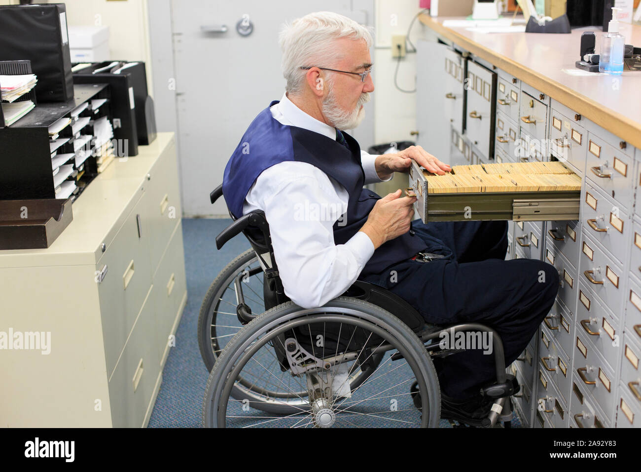 Man with Muscular Dystrophy in a wheelchair working in an office Stock