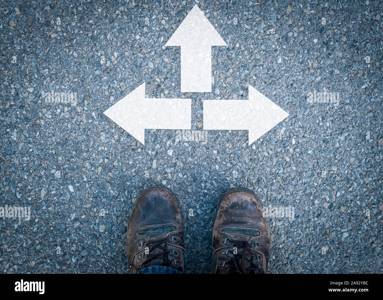 well worn walking shoes on asphalt road with tree arrows in different directios ,concept decisions direction. Stock Photo