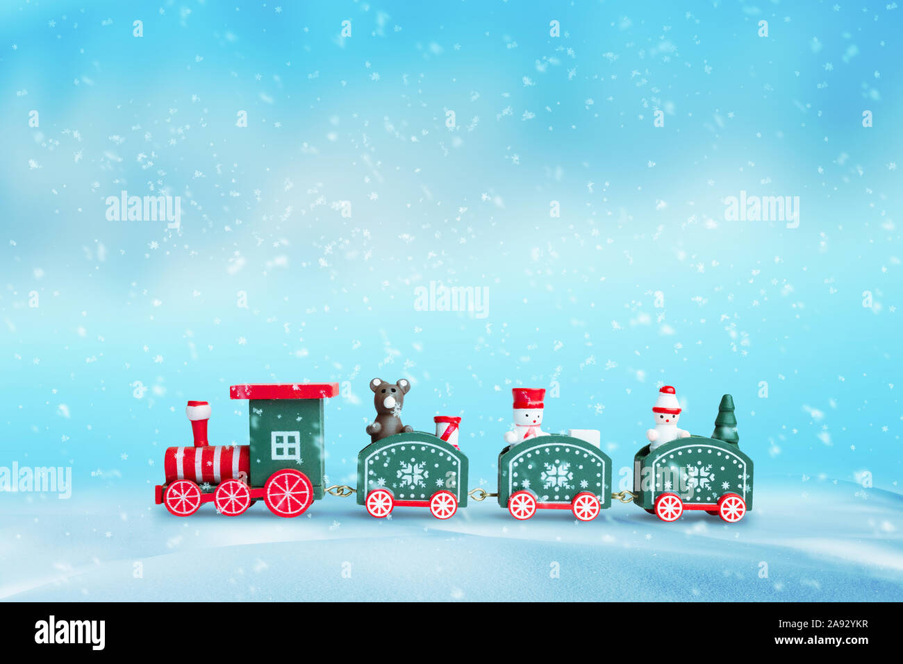 Cute train in the snow. Christmas; New Year background. Wooden toy with a bear and two snowshoes in wagons. Blue background. Stock Photo