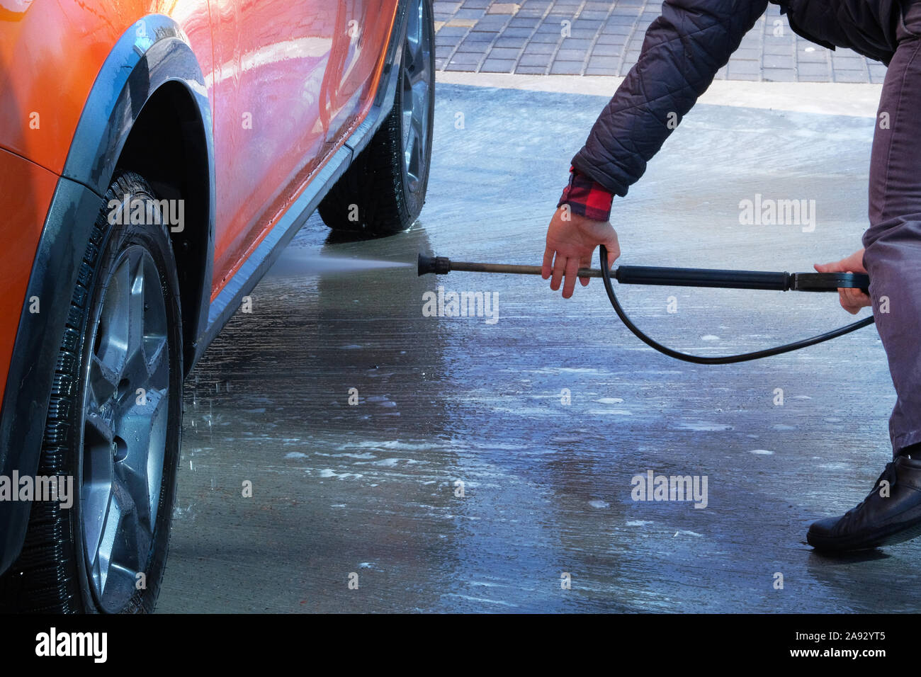 Cleaning with water at self-service car wash. Man washes his orange car at car wash in outdoors. Stock Photo
