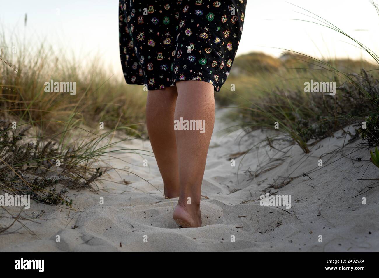Woman in black dress with feet buried in sand seen from waist down Stock Photo