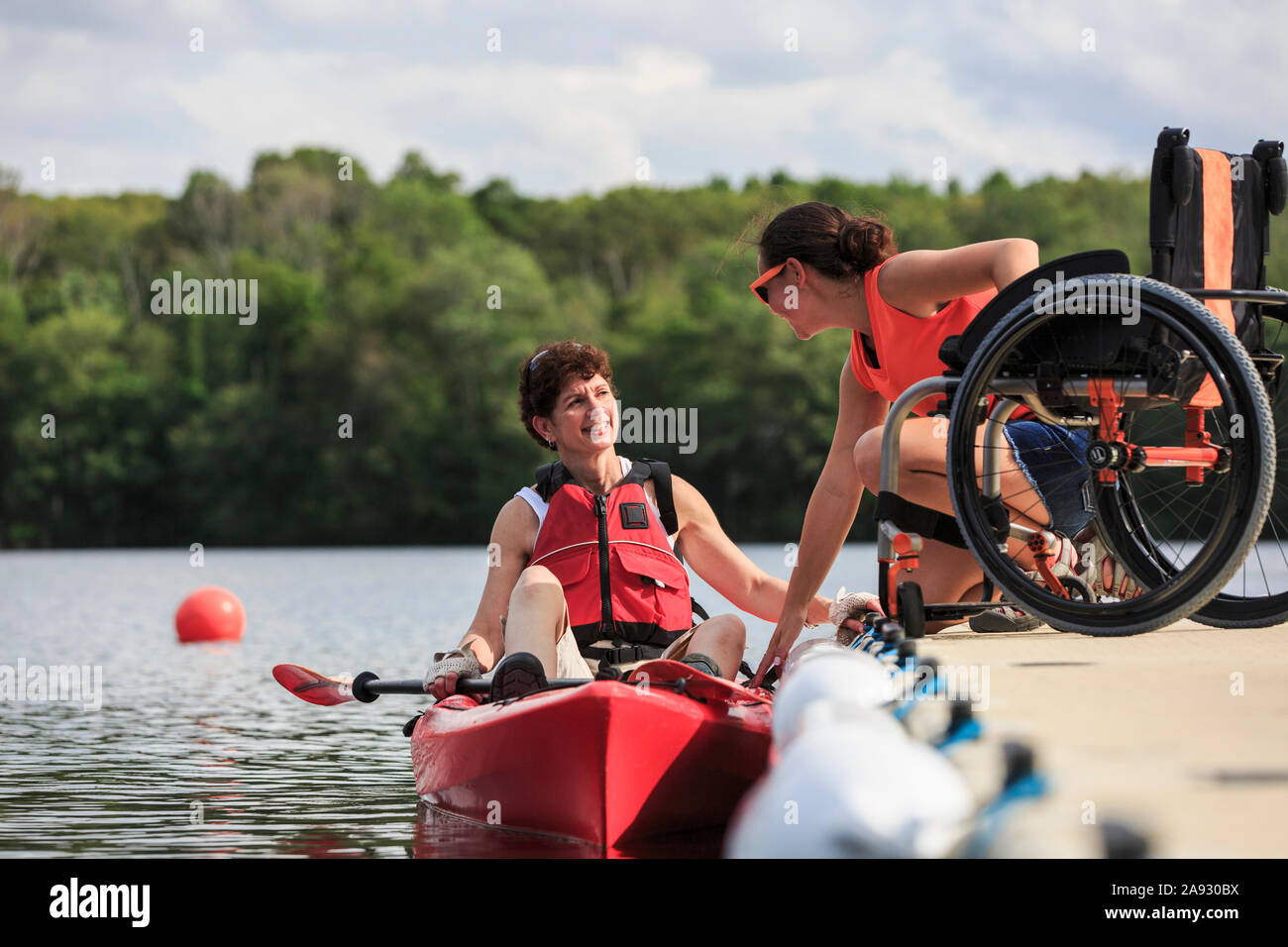 Instructor helping a woman with a Spinal Cord Injury use a kayak Stock