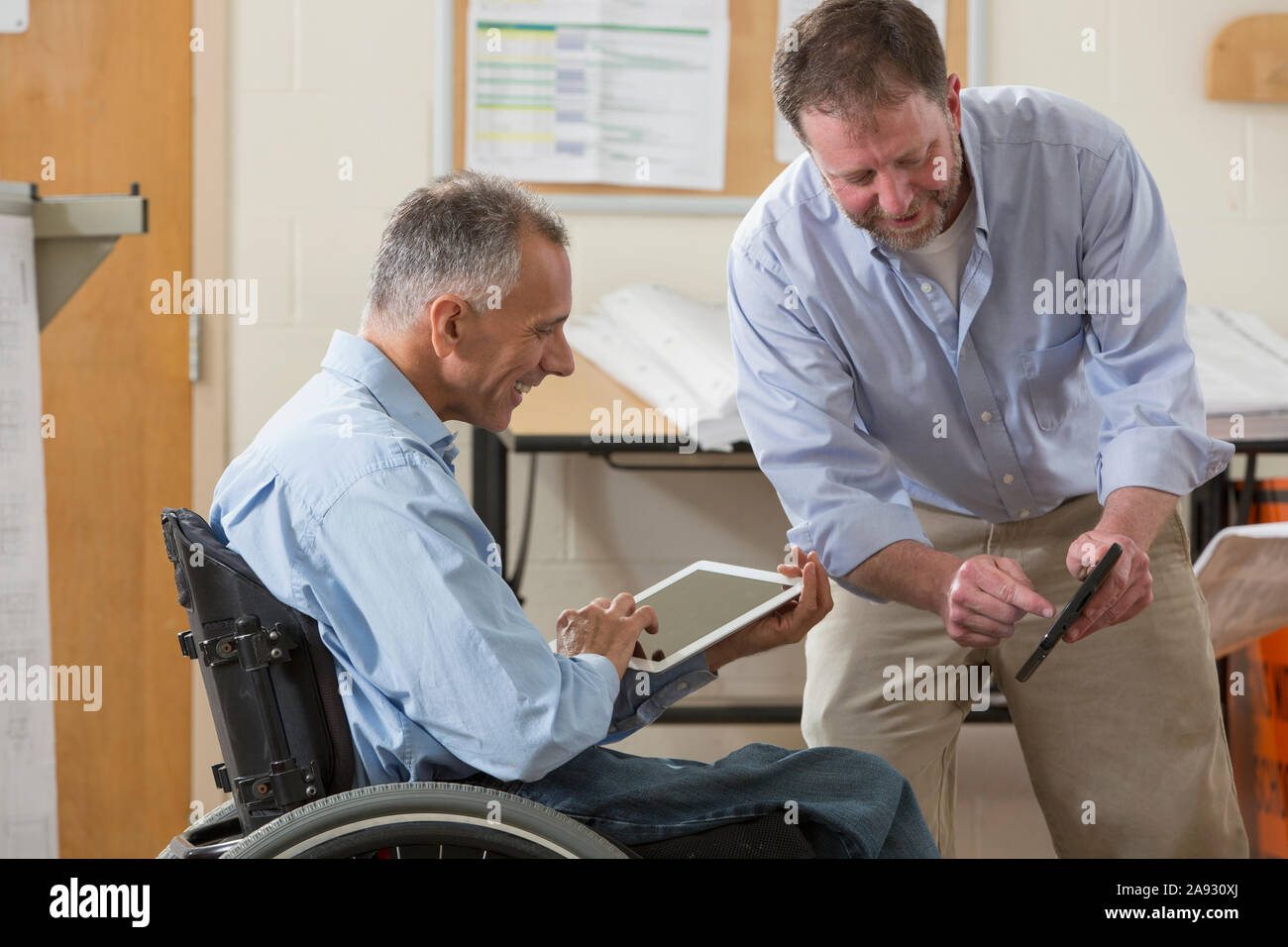 Two project engineers using their tablets to check job site plans, one in a wheelchair with a Spinal Cord Injury Stock Photo