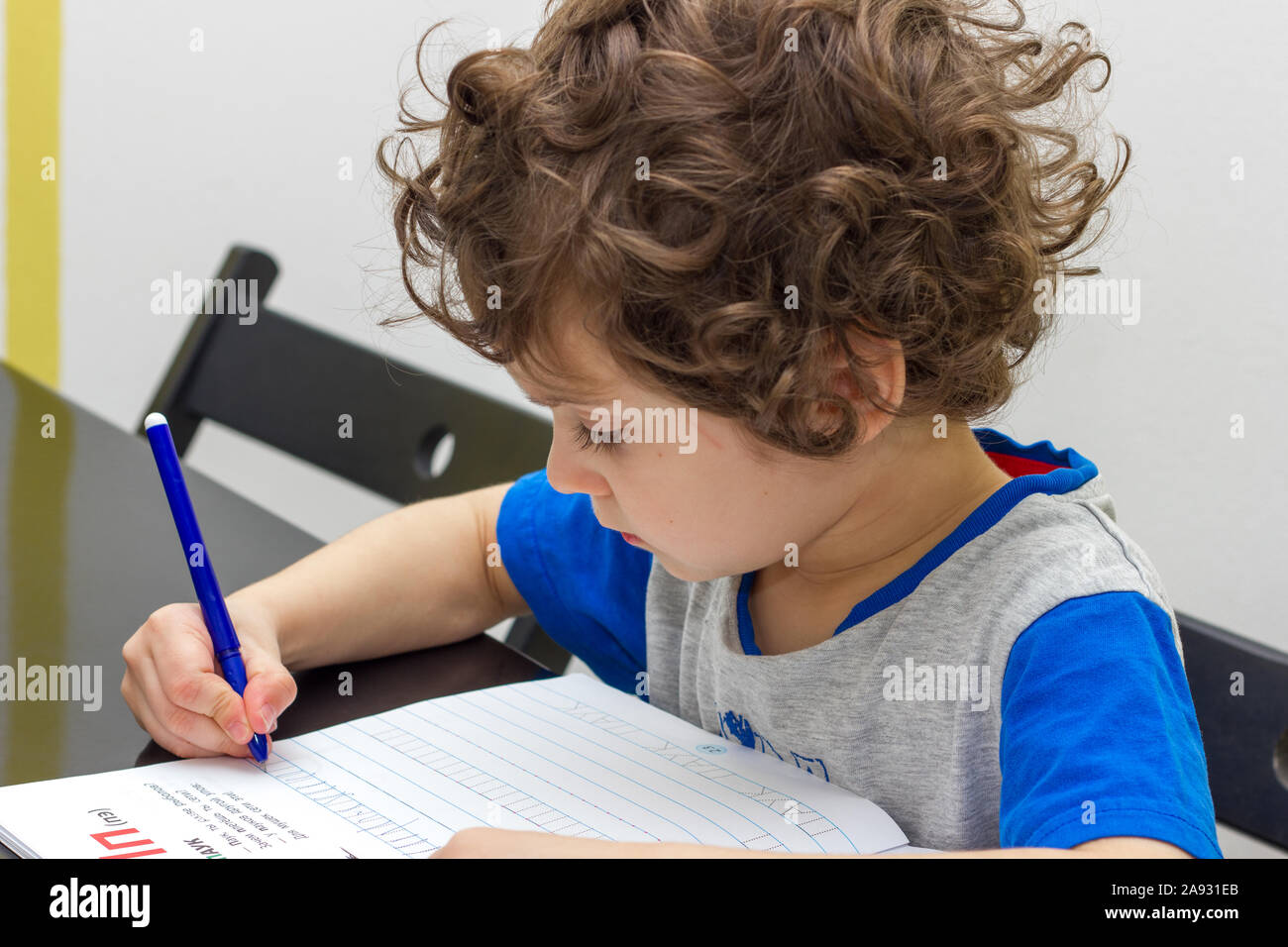Happy curly boy sits at a table and write Stock Photo