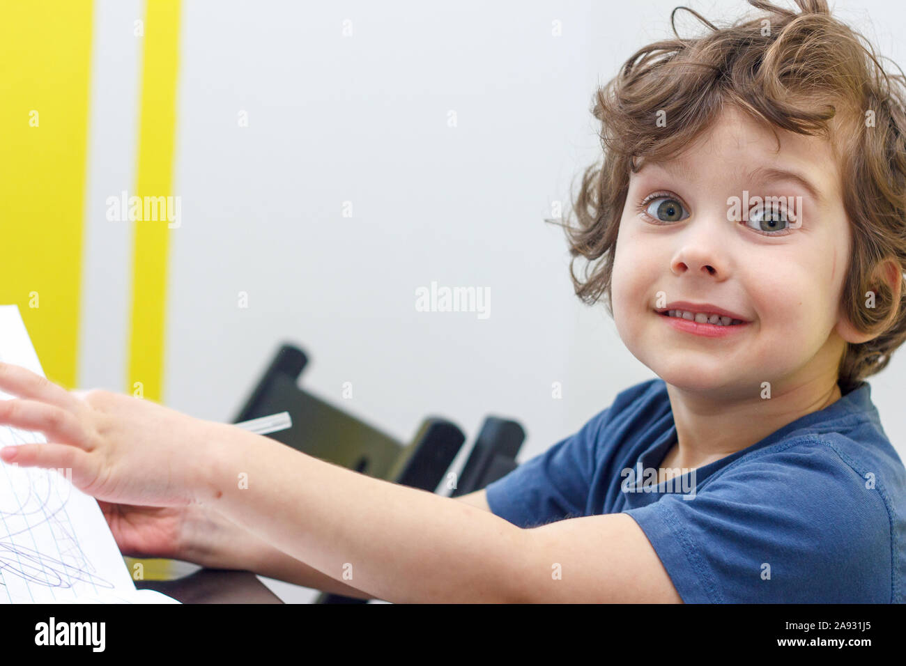 Happy curly boy smiles and sits at a table Stock Photo