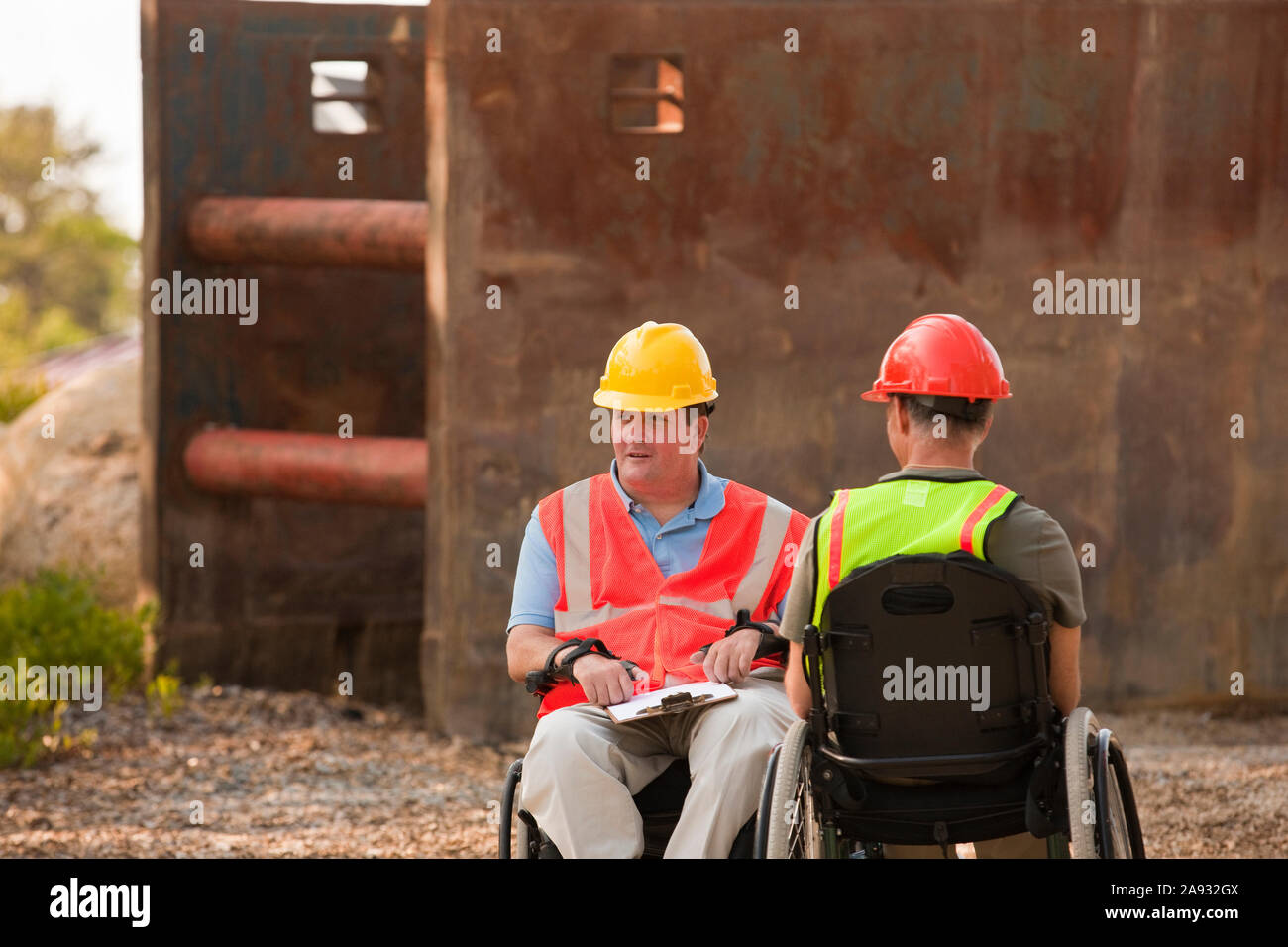 Project engineers in wheelchairs discussing plans on site Stock Photo