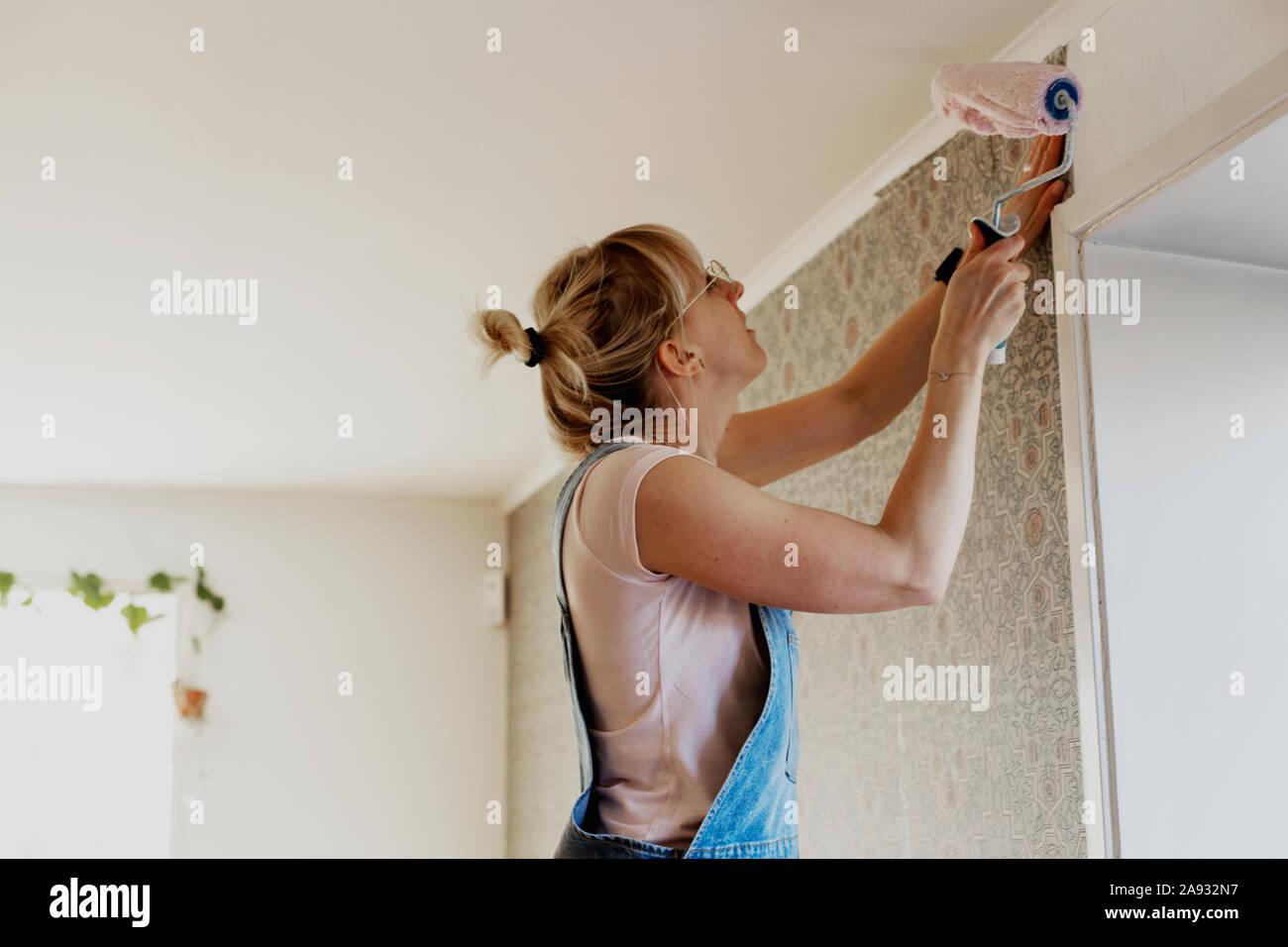 Woman sticking wallpaper on wall Stock Photo