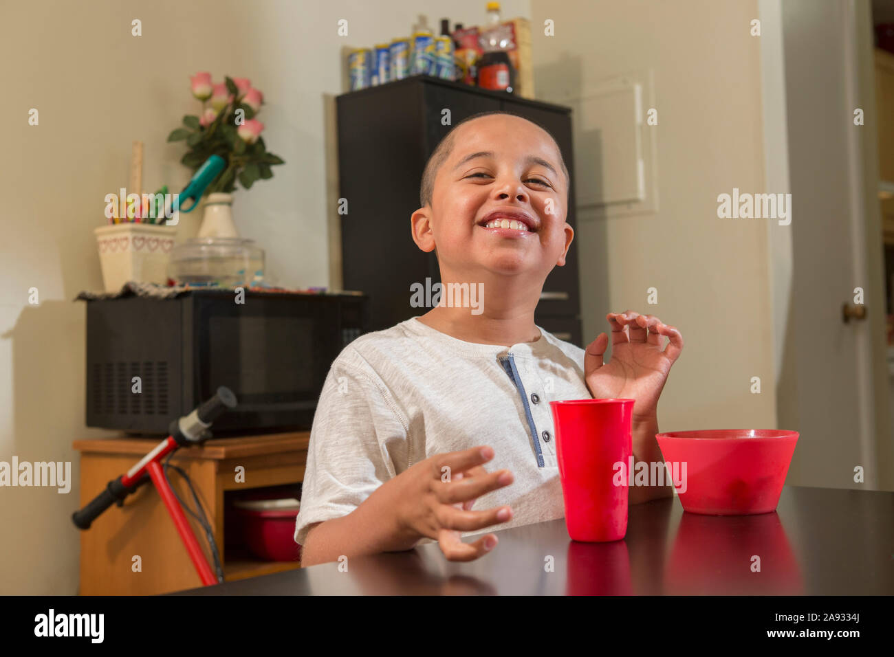 Happy Hispanic boy with Autism eating in his kitchen Stock Photo