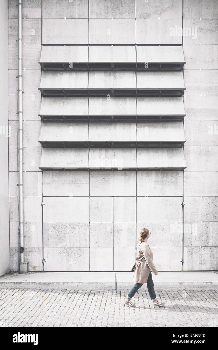 Woman walking in front of concrete building Stock Photo